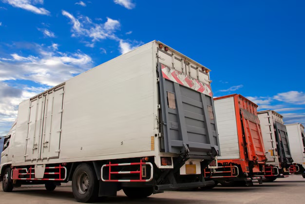 Box trucks with tail lifts parked in a row under a blue sky